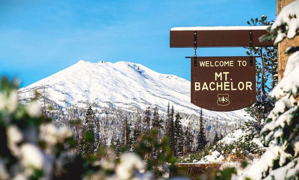 The Mt. Bachelor sign and ski resort in the background on a sunny day.