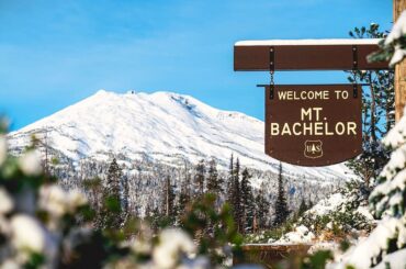 The Mt. Bachelor sign and ski resort in the background on a sunny day.