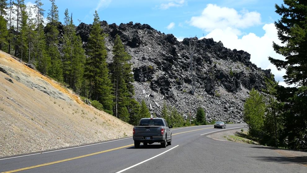 A car driving on the Cascade Lakes Scenic Byway in front of a lava field.