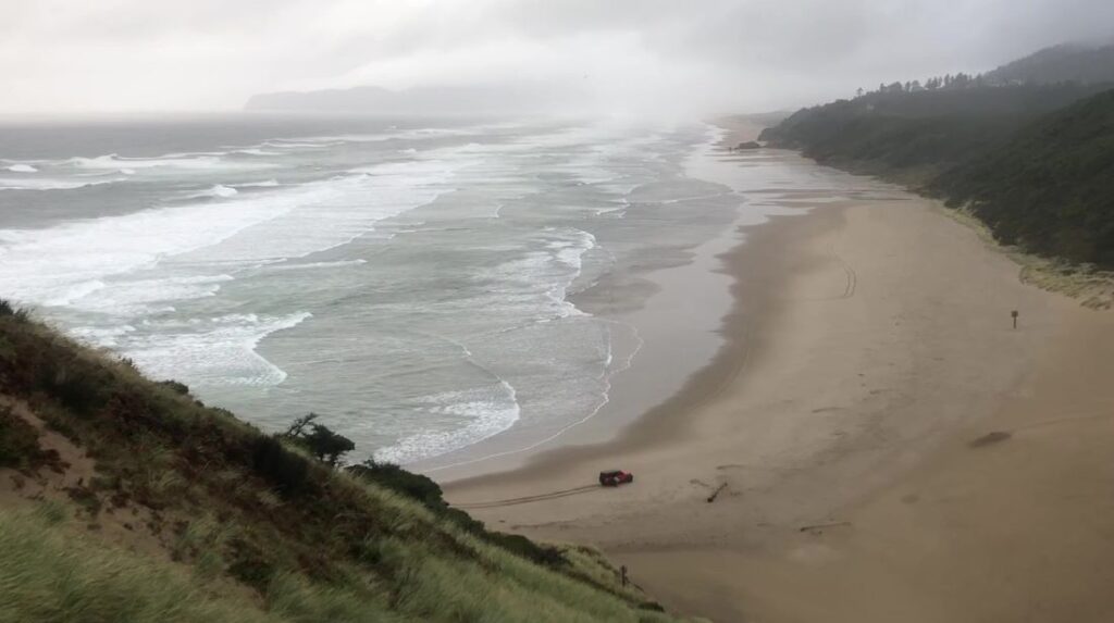 A car driving on McPhillips beach at Pacific City Oregon.